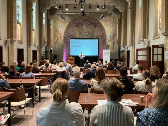 Mérijn Stam van theFactor.e presenteert in de kapel van Kontakt der Kontinenten de resultaten van het LLO-benchmarkonderzoek aan deelnemers van 33 mbo- en hbo-instellingen. Op het scherm staat de dia “Interviews met de doelgroep & deskresearch”, passend bij het inhoudelijke ochtendprogramma.